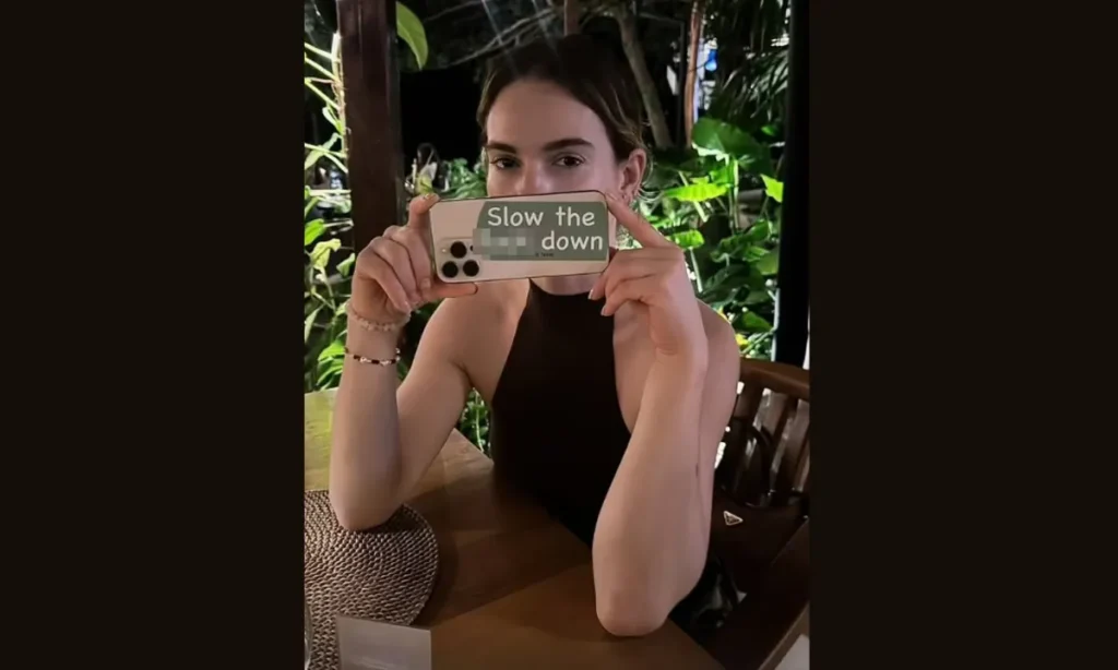 Lily James sidder ved et bord, hvor der på hendes telefon står "Slow the F*ck down"